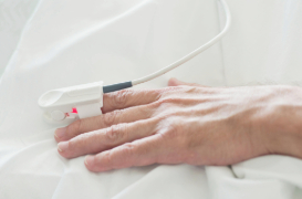 Close-up of hands with an adult patient wearing a red pulse oximeter.